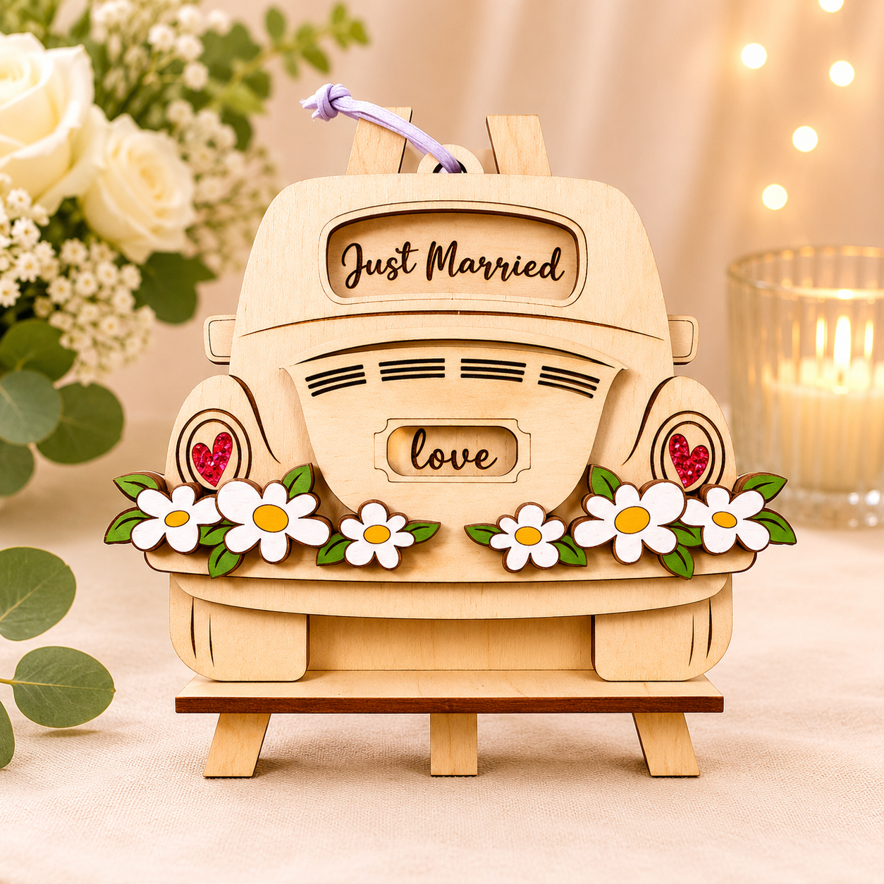 Handmade wood just married car gift card holder shaped like a vintage bug with "Just Married" lettering, a white daisy bumper, and red gem taillights, hanging from a purple leather cord on a small wooden easel beside white roses and a candle