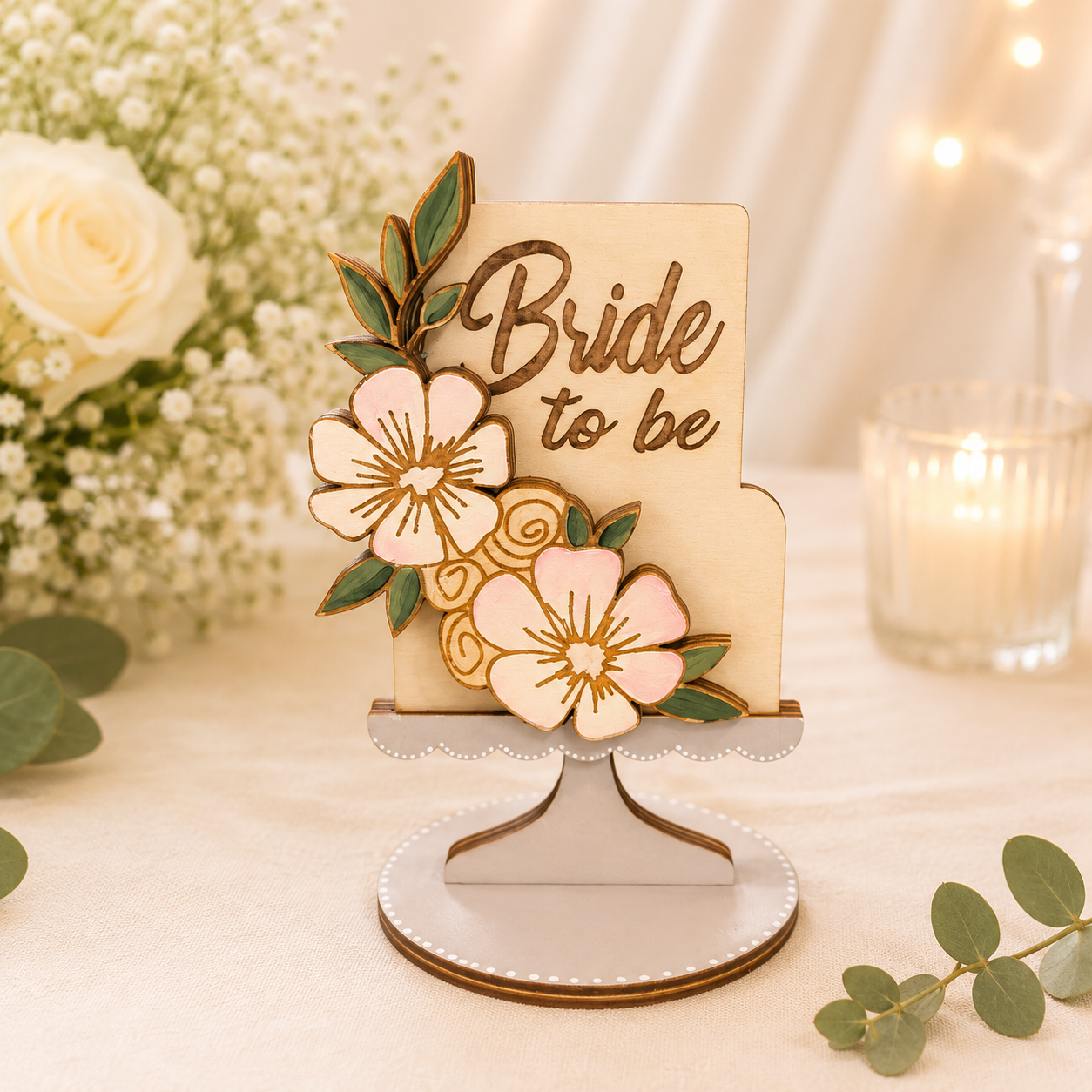 Handmade wood bride-to-be gift card holder shaped like a tiered floral cake on a cake stand, hand-painted with blush pink and cream flowers and green leaves, "Bride to be" engraved on the front, 