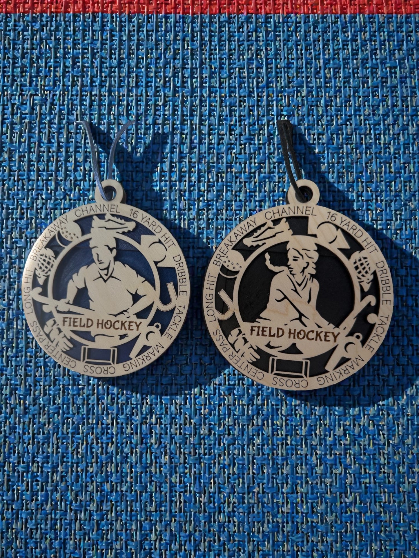 Two silver field hockey medallions on a blue textured background