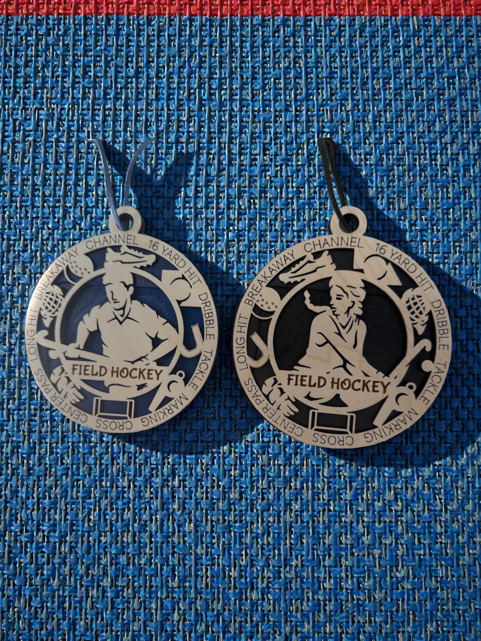 Two silver field hockey medallions on a blue textured background