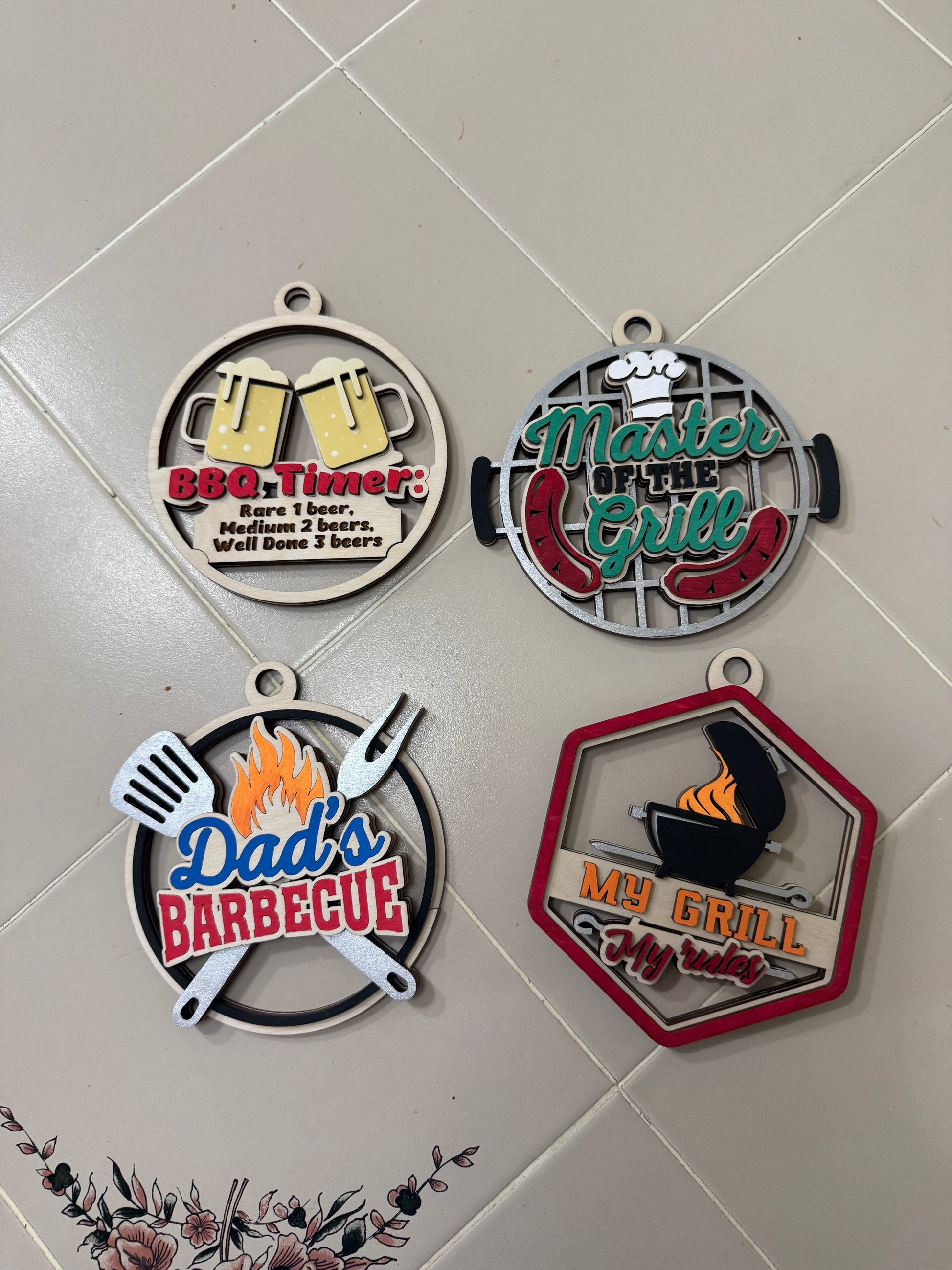 Four handmade layered wood BBQ medallion gift card holders in round and hexagon shapes, featuring grill-themed designs including BBQ Timer, Master of the Grill, Dad's Barbecue, and My Grill My Rules, made from 3 layers of Baltic birch with leather hanging cord