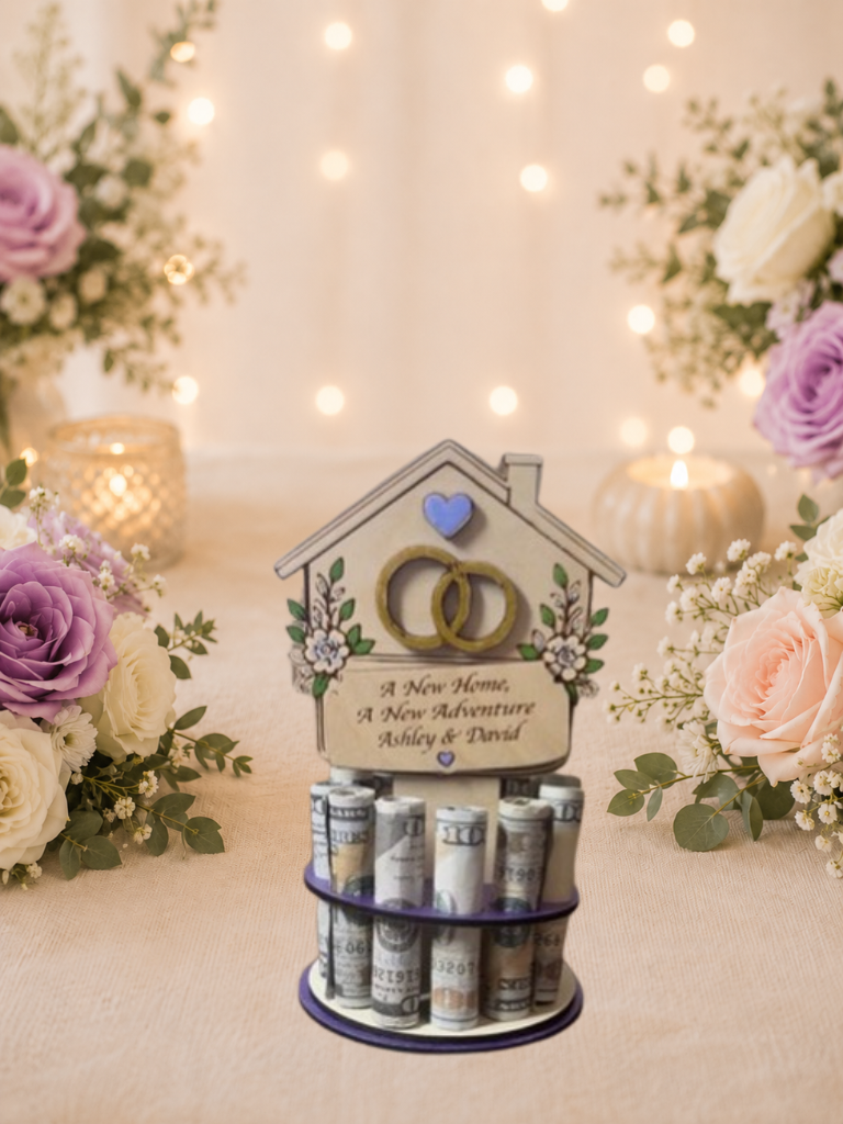 Premium handmade wood new home money tree with house-shaped topper featuring interlocking wedding rings, purple heart accent, and hand-painted florals with personalized text reading "A New Home, A New Adventure" and "Ashley & David," displayed on a single-tiered purple circular base holding 12 rolled bills, surrounded by purple and blush roses with candlelight